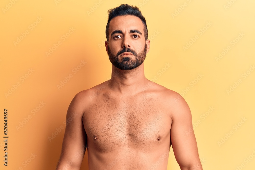 Young hispanic man standing shirtless with serious expression on face. simple and natural looking at the camera.