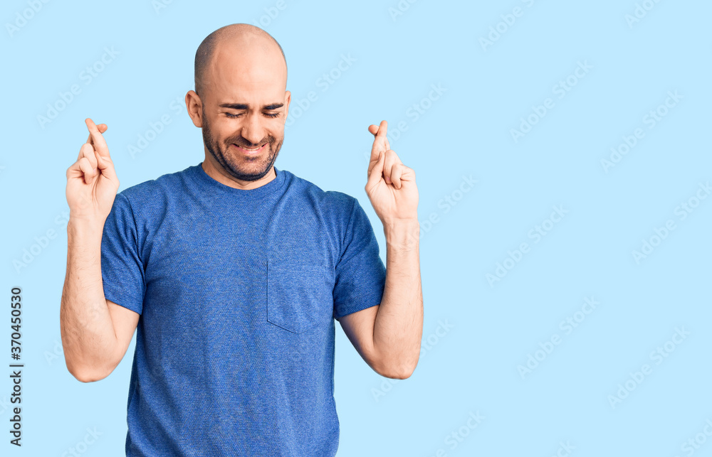 Young handsome man wearing casual t shirt gesturing finger crossed smiling with hope and eyes closed. luck and superstitious concept.