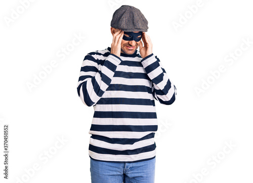 Young handsome man wearing burglar mask with hand on head, headache because stress. suffering migraine. © Krakenimages.com