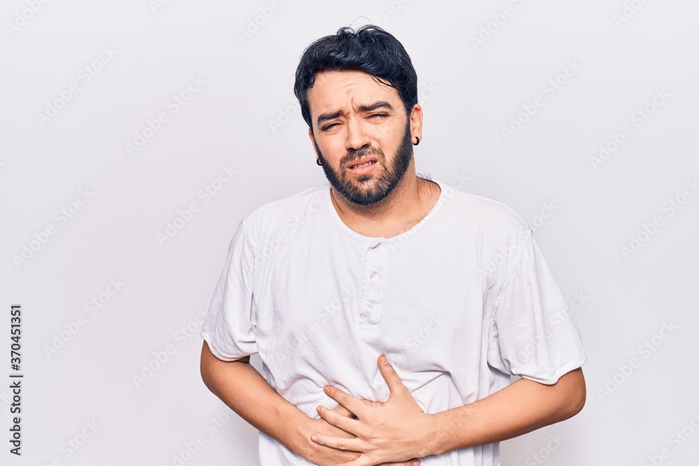 Young hispanic man wearing casual clothes with hand on stomach because indigestion, painful illness feeling unwell. ache concept. Young hispanic man wearing casual clothes with hand on stomach because indigestion, painful illness feeling unwell. ache concept.