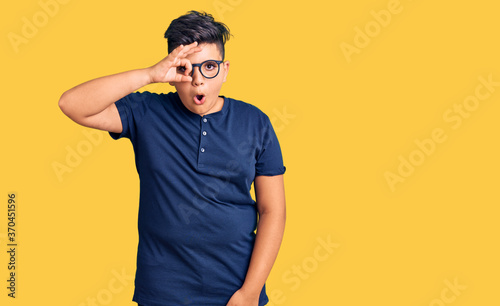 Little boy kid wearing casual clothes and glasses doing ok gesture shocked with surprised face, eye looking through fingers. unbelieving expression.