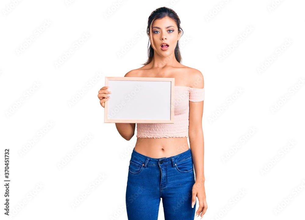 Young beautiful woman holding empty white chalkboard scared and amazed with open mouth for surprise, disbelief face Young beautiful woman holding empty white chalkboard scared and amazed with open mouth for surprise, disbelief face