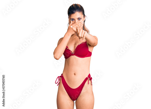 Young beautiful woman wearing bikini laughing at you, pointing finger to the camera with hand over mouth, shame expression © Krakenimages.com