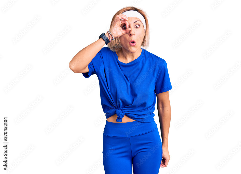 Fototapeta premium Young blonde woman wearing sportswear doing ok gesture shocked with surprised face, eye looking through fingers. unbelieving expression.