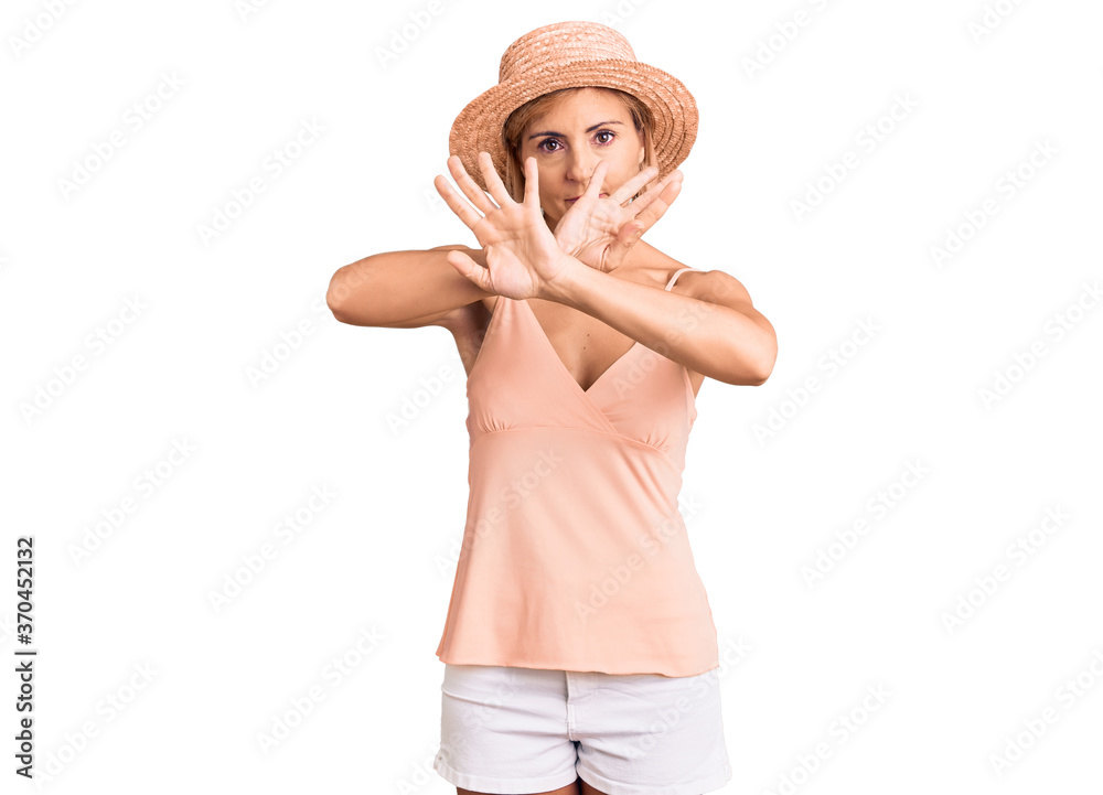 Young blonde woman wearing summer hat rejection expression crossing arms and palms doing negative sign, angry face Young blonde woman wearing summer hat rejection expression crossing arms and palms doing negative sign, angry face