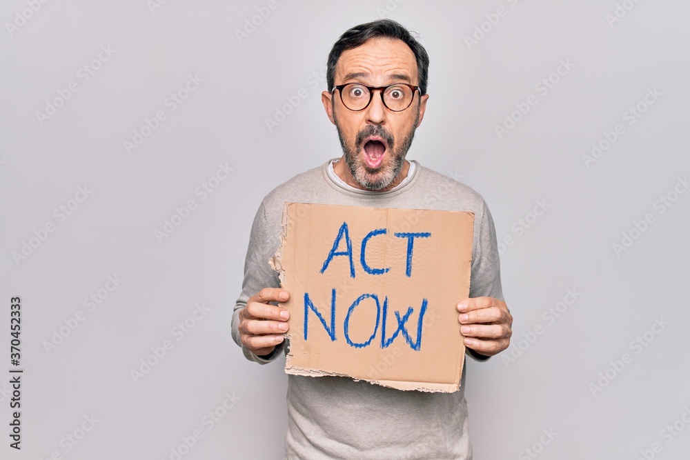 Middle age handsome man asking for rights holding banner with act now message scared and amazed with open mouth for surprise, disbelief face Middle age handsome man asking for rights holding banner with act now message scared and amazed with open mouth for surprise, disbelief face