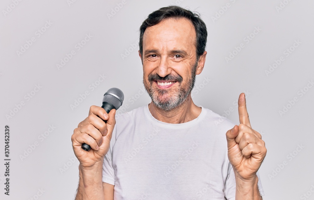 Middle age handsome singer man singing using microphone over isolated white background smiling with an idea or question pointing finger with happy face, number one Middle age handsome singer man singing using microphone over isolated white background smiling with an idea or question pointing finger with happy face, number one