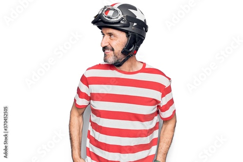 Middle age handsome motorcyclist man wearing moto helmet over isolated white background looking to side, relax profile pose with natural face and confident smile.