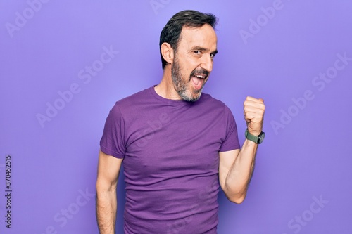 Middle age handsome man wearing casual purple t-shirt standing over isolated background pointing thumb up to the side smiling happy with open mouth