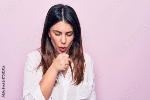 Young beautiful brunette woman wearing elegant shirt standing over isolated pink background feeling unwell and coughing as symptom for cold or bronchitis. Health care concept.