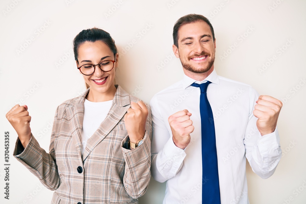 Beautiful couple wearing business clothes very happy and excited doing winner gesture with arms raised, smiling and screaming for success. celebration concept. Beautiful couple wearing business clothes very happy and excited doing winner gesture with arms raised, smiling and screaming for success. celebration concept.