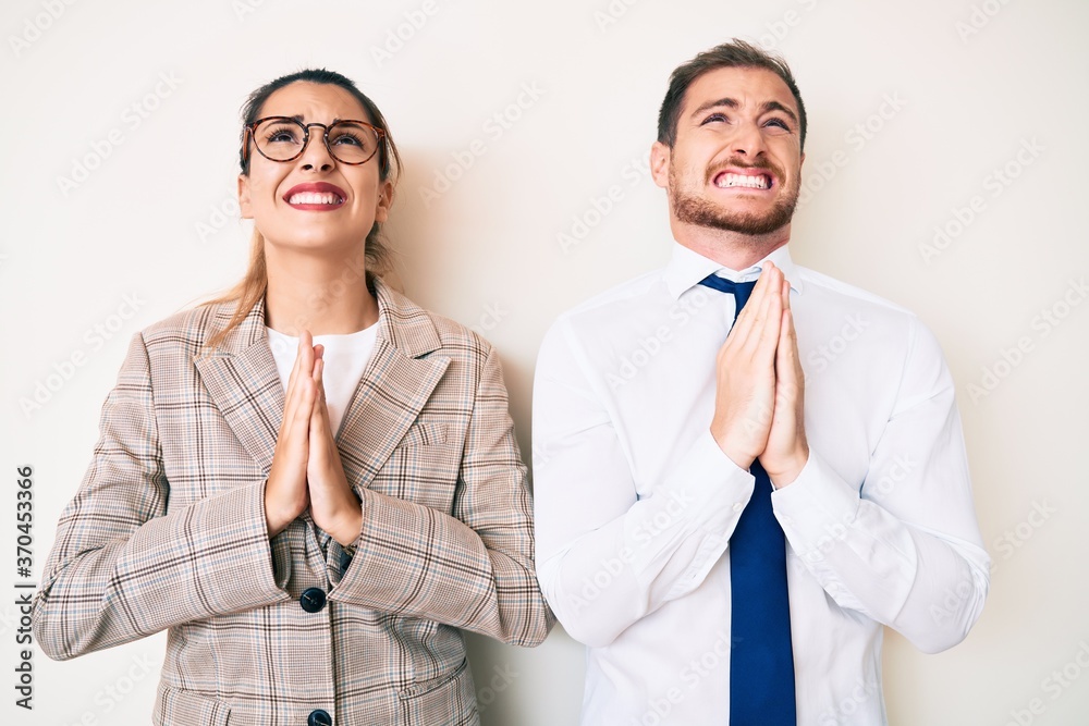 Beautiful couple wearing business clothes begging and praying with hands together with hope expression on face very emotional and worried. begging. Beautiful couple wearing business clothes begging and praying with hands together with hope expression on face very emotional and worried. begging.
