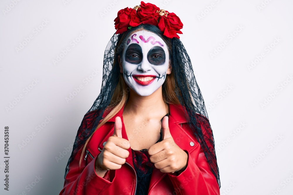 Woman wearing day of the dead costume with thumbs up doing ok sign smiling with a happy and cool smile on face. showing teeth. Woman wearing day of the dead costume with thumbs up doing ok sign smiling with a happy and cool smile on face. showing teeth.