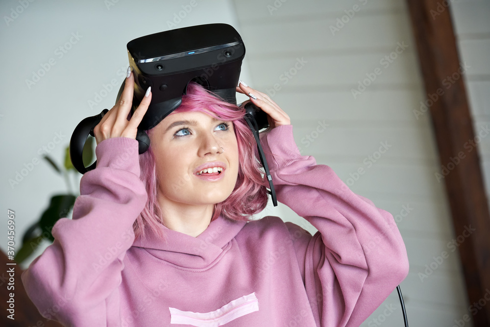 Excited hipster teen girl pink hair wears vr headset holds controller  looking up amazed with digital innovation virtual reality 3D 360 video  gaming entertainment experience. Head shot face portrait. Stock Photo