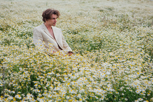 Tall handsome man sitting on a white chair in camomile flowers field