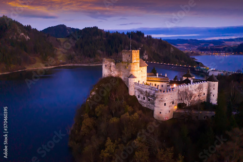 Fototapeta Naklejka Na Ścianę i Meble -  Scenic view of ancient fortified Dunajec Castle on top of hill above Czorsztyn lake in Polish city of Niedzica at dusk..