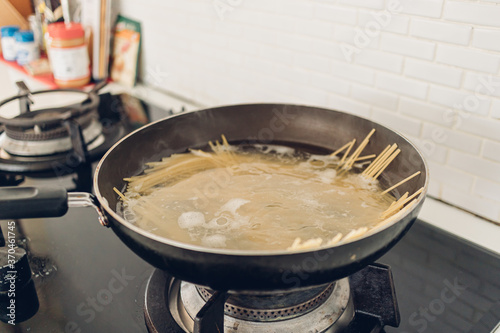 Image of boiling spaghetti with the pan in white kitchen.