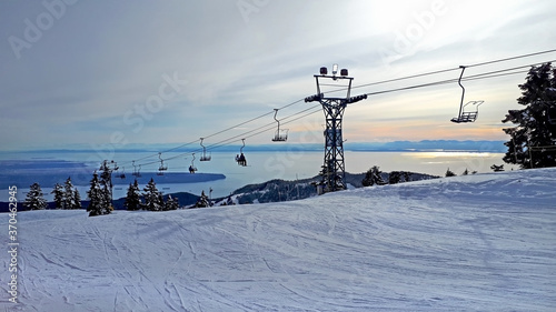 Cypress mountain in West Vancouver, BC. The romantic sunset. The view on the snowy downhill and ski chairlift with ocean / sea and island in the background.