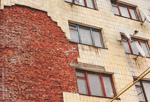 Old high-rise building with broken windows, crumbling walls covered with cracks and scratches