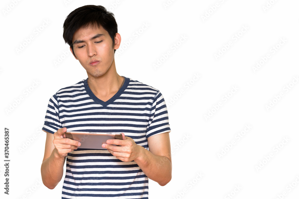 Studio shot of young handsome Asian man using digital tablet isolated against white background