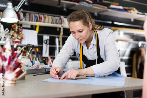 Smiling woman tailor working with marker for modeling clothes at atelier