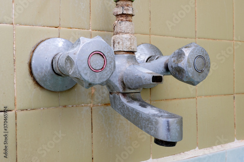White chalky limescale stains and soap residue deposits being formed on an unclean bathtub shower metal faucet or dirty water tap, closeup side view.