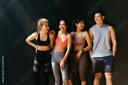 Happy smiling man and women having fun talking in gym. Group of young people relaxing in gym after workout training with black background.