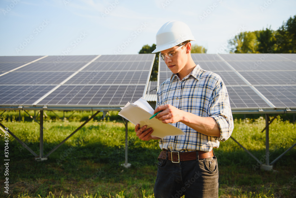 The portrait of a young engineer checks photovoltaic solar panels. Concept: renewable energy, technology, electricity, service, green power.