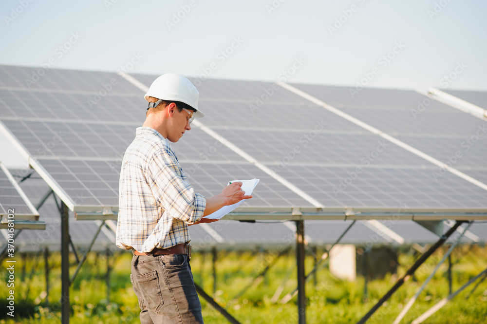 The portrait of a young engineer checks photovoltaic solar panels. Concept: renewable energy, technology, electricity, service, green power.