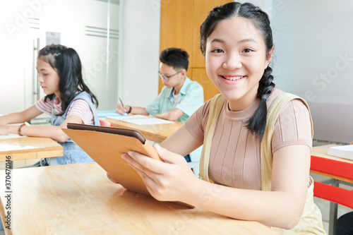 Portrait of smiling teenage Vietnamese girl using digital tablet in class