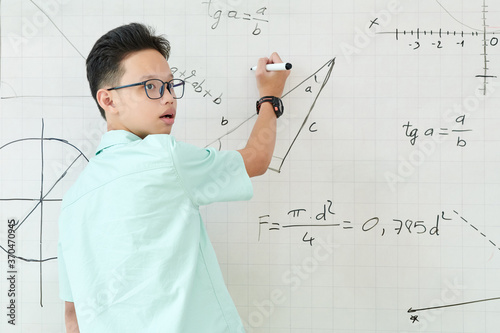 Vietnamese schoolboy listening to advice of classmate when solving geometry task and writing on whiteboard
