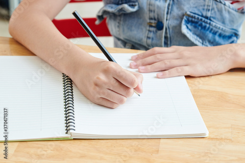 Close-up image of schoolgirl writing essay in copybook at her desk or drawing sketch for school project