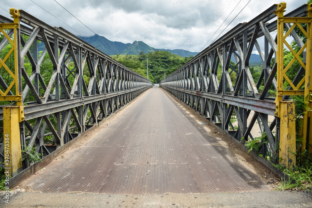 Metal bridge over a river that borders Honduras and El Salvador with mountains in the background