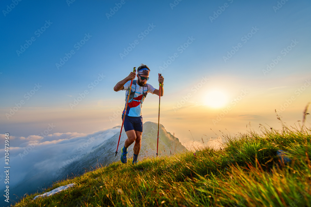 Man with poles in the mountains with sunset behind