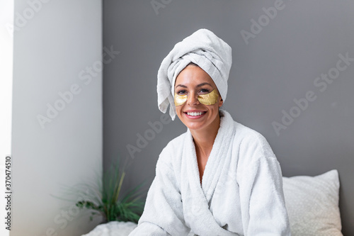 Young woman face with Gold Cosmetics mask, Eye Patches and perfect skin wearing bath towel and bathrobe, sitting on the bed