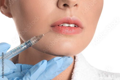 Beautiful young woman receiving injection of filler on white background, closeup