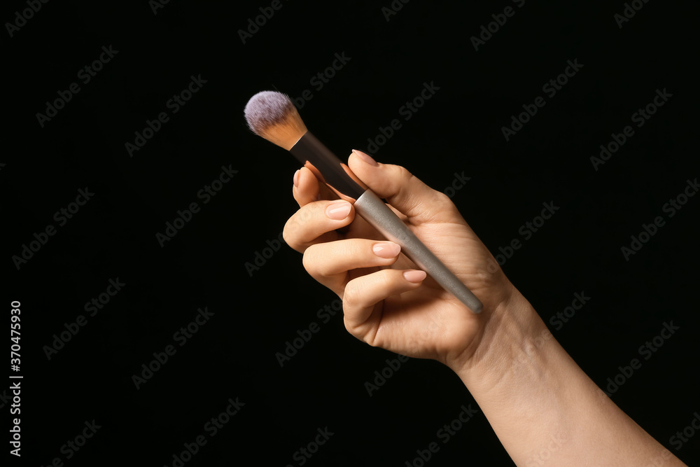 Hand with beautiful manicure holding makeup brush on dark background - obrazy, fototapety, plakaty 