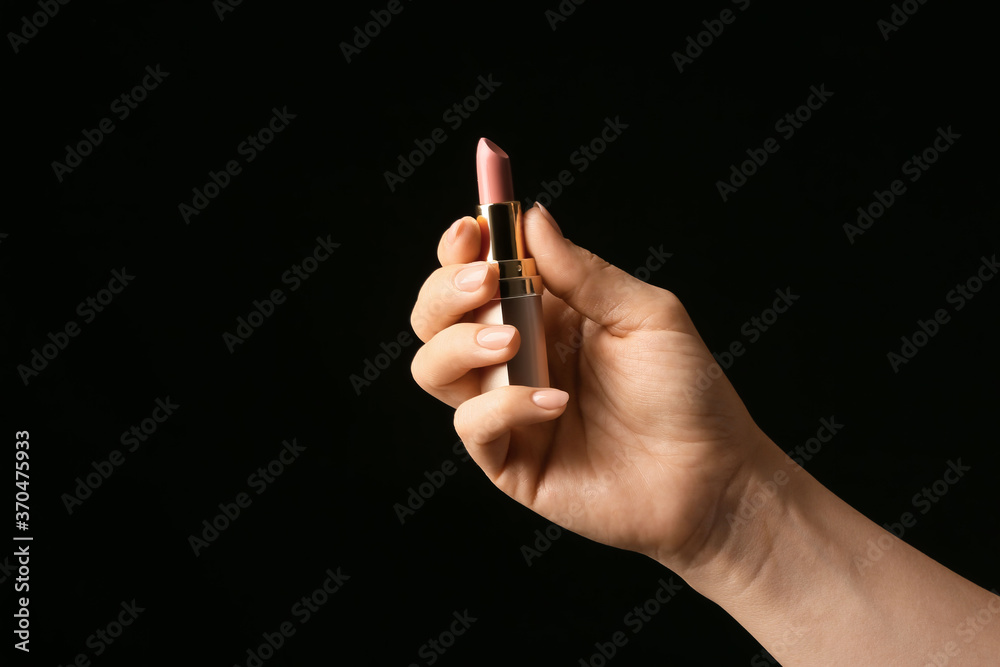 Hand with beautiful manicure holding lipstick on dark background - obrazy, fototapety, plakaty 