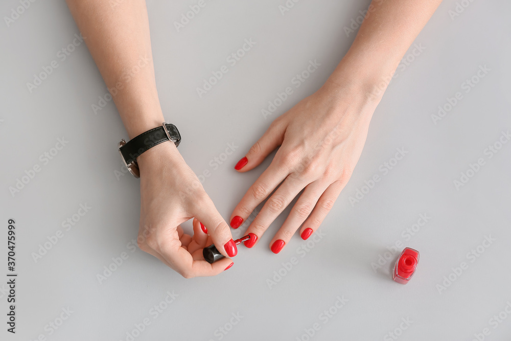 Woman applying nail polish against grey background - obrazy, fototapety, plakaty 