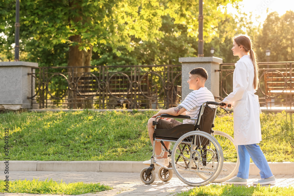 Doctor and young man in wheelchair outdoors Doctor and young man in wheelchair outdoors