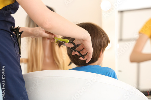 Female hairdresser working with little boy in salon