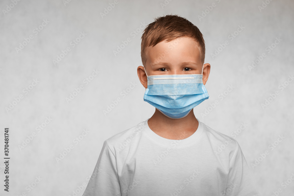 Smiling boy weared in surgical mask and white t-shirt on a white background.   Covid-19, flu, or pollution protection concept. With place for your text.