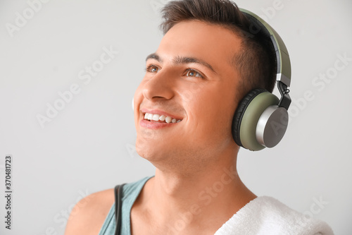 Sporty young man with headphones on light background