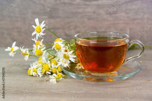 fresh herbal tea in transparent glass cup with camomile flowers
