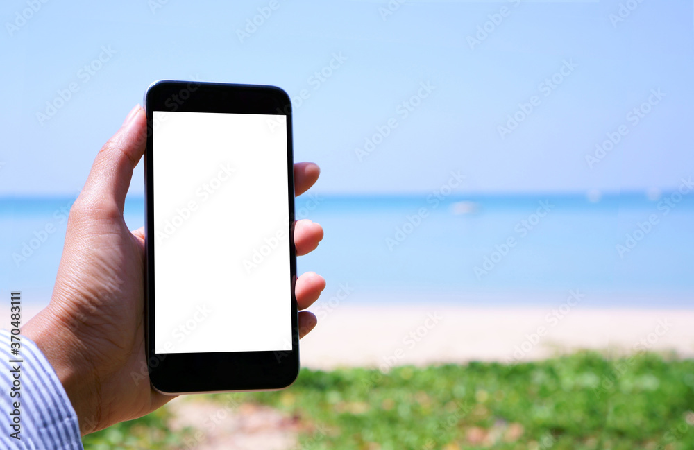A white screen mobile smartphone on a woman's hand in front the white sand beach blue sea and sky