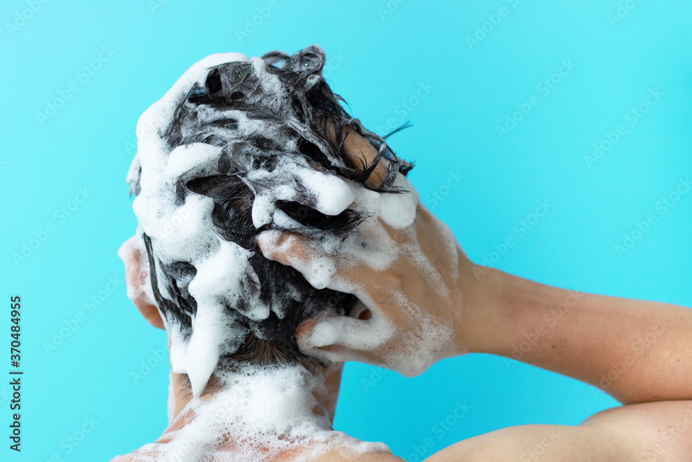 A man washes his head with shampoo on blue background, a copy of the space