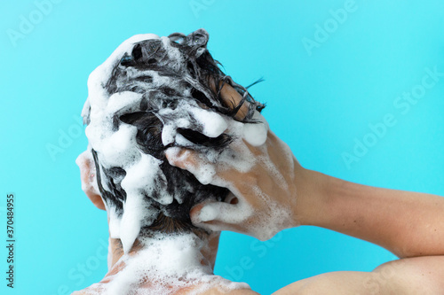 A man washes his head with shampoo on blue background, a copy of the space