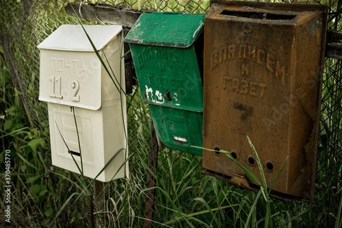 Vintage rustic mailboxes of different colors pinned on a fence.