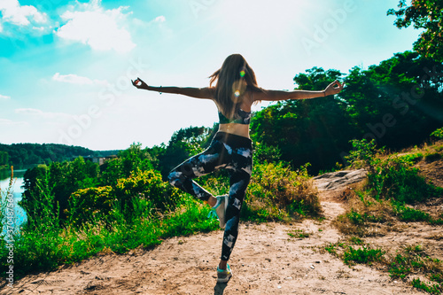 Woman Doing Yoga On Mountain Against Sky and Sun. Hard light. Silhouette of girl doing outdoor sport stretch. photo