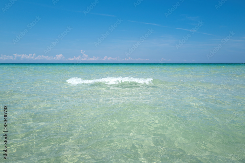 Soft blue ocean wave on clean sandy beach. Tropical paradise beach with white sand. Beautiful beach with palm trees and moody sky.